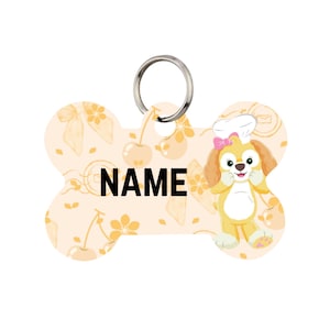 May include: Bone-shaped pet tag with a cartoon chef dog illustration. The tag has a light peach background with a pattern of cherries and flowers. The word "NAME" is printed in bold black letters.