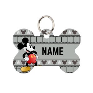 Könnte beinhalten: Knochenförmiger Haustieranhänger mit Mickey Mouse. Der Anhänger ist grau mit einem Filmstreifen-Design und Mickey Mouse-Symbolen. Der Name "NAME" ist in Schwarz gedruckt. Ein silberner Ring ist zur Befestigung am Halsband angebracht.