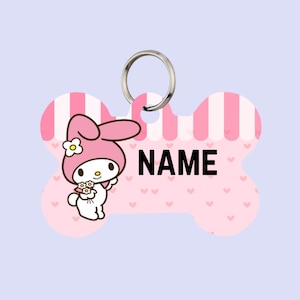 May include: A pink bone-shaped pet tag with a cartoon character and the word "NAME" in black. The tag has a silver ring for attachment. The background is light pink with hearts and stripes.