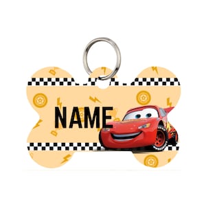 Puede incluir: Etiqueta para mascotas en forma de hueso con una imagen de dibujos animados de un coche de carreras rojo y la palabra "NAME" en letras negras. La etiqueta tiene un fondo amarillo con rayos y banderas de carreras.