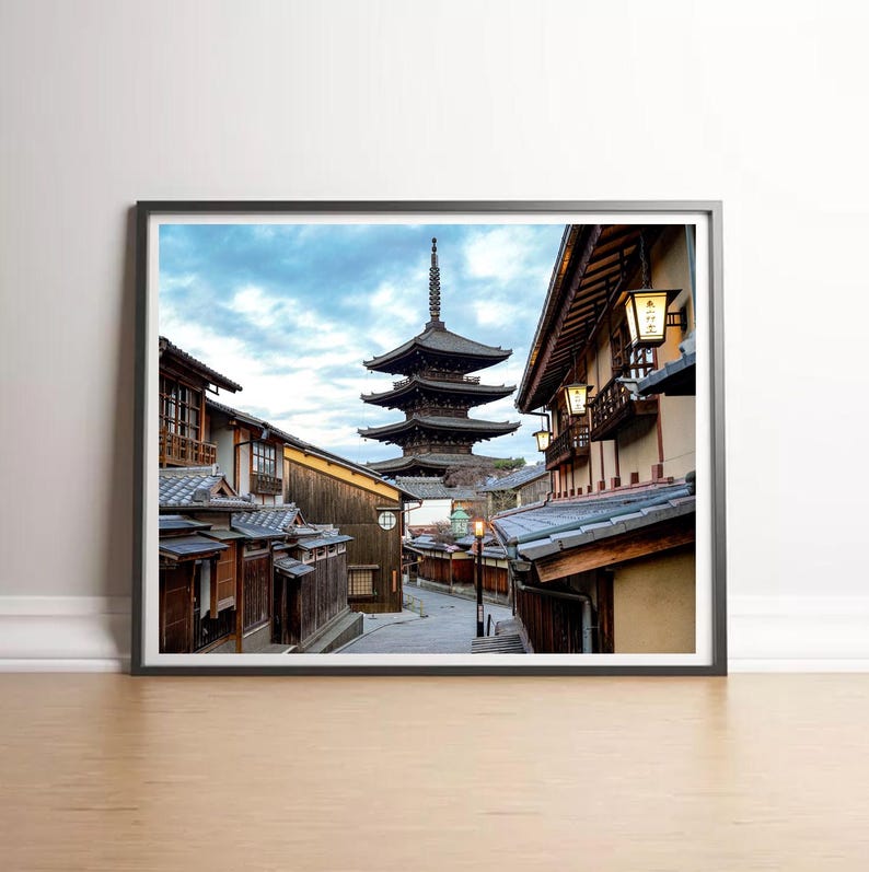 May include: A photograph of a traditional Japanese street with a pagoda in the background. The street is lined with wooden buildings and lanterns. The sky is cloudy and the scene is peaceful.