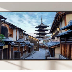 May include: A narrow street lined with traditional Japanese wooden buildings, with a five-storey pagoda in the distance. The buildings have dark wood siding and tiled roofs. The street is paved with grey stones and there are trees and plants growing along the sides.