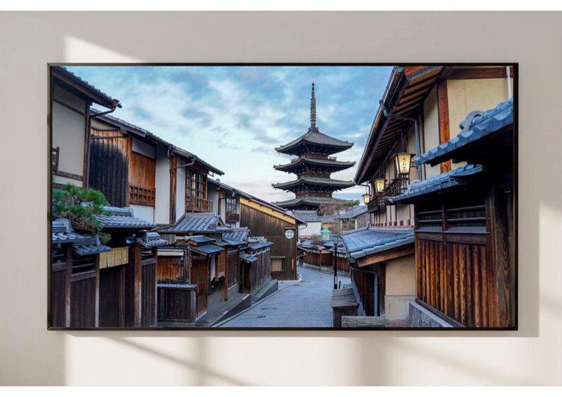 May include: A narrow street lined with traditional Japanese wooden buildings, with a five-storey pagoda in the distance. The buildings have dark wood siding and tiled roofs. The street is paved with grey stones and there are trees and plants growing along the sides.