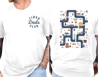 May include: White t-shirt with a navy blue graphic on the front that reads "Tired Dads Club." The back of the shirt features a colorful illustration of a road map with cars, houses, and trees.
