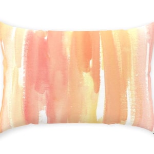Op de afbeelding: Rechthoekig decoratief kussen met een aquarelontwerp. Het kussen heeft verticale penseelstreken in tinten perzik, oranje en geel. Het ontwerp is geplaatst tegen een witte achtergrond, waardoor een zachte, artistieke esthetiek ontstaat.