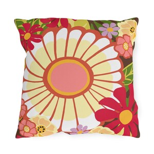 May include: Square throw pillow with a large, stylized yellow and white flower at the center, surrounded by red, pink, and yellow flowers on a brown background. The pillow has a floral pattern.