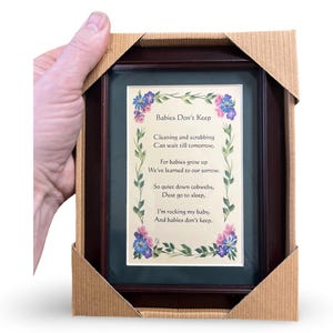 Pode incluir: Um poema emoldurado com uma moldura de madeira escura e um passe-partout verde. O poema &eacute; intitulado "Babies Don't Keep" e est&aacute; escrito em uma fonte caprichosa com ilustra&ccedil;&otilde;es florais. O poema diz: "Limpar e esfregar podem esperar at&eacute; amanh&atilde;, porque os beb&ecirc;s crescem, aprendemos isso com pesar. Ent&atilde;o, sil&ecirc;ncio, teias de aranha, p&oacute; v&aacute; dormir, estou embalando meu beb&ecirc;, e os beb&ecirc;s n&atilde;o ficam."