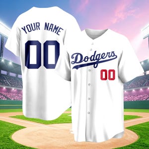 May include: A white baseball jersey featuring the blue script text Dodgers on the front with a red number 00. The back of the jersey displays the text YOUR NAME in blue above the large blue number 00. The shirt has a button-down front closure.