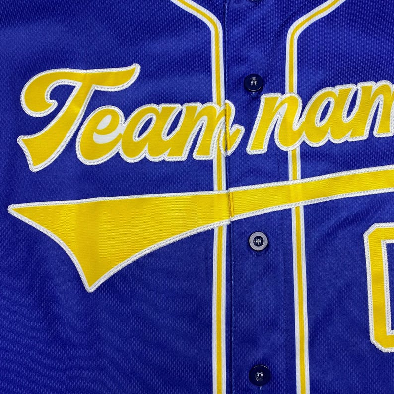 May include: A royal blue button-down baseball jersey featuring the text Team name in yellow script with white trim. The jersey includes a yellow swoosh graphic across the front, vertical yellow and white piping, and dark blue buttons.