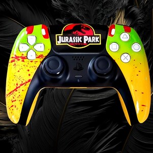 May include: A black and yellow PlayStation 5 controller with a Jurassic Park theme. The controller has a black center with the Jurassic Park logo and yellow and green sides with red splatter details.