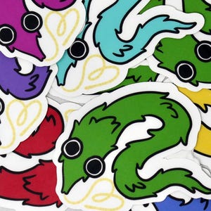 May include: A selection of colourful worm stickers in shades of purple, blue, green, and red. Each sticker features a cartoon worm with large black eyes and a yellow heart design. The stickers are on a white background.