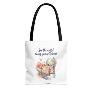 May include: A white tote bag with black handles featuring a watercolor illustration of a brown suitcase, a globe, a passport, a coffee mug, and birds. The text "See the world, bring yourself home" is printed in dark blue script above the travel items.
