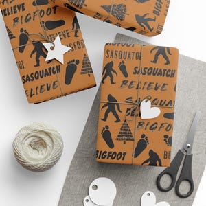 May include: Orange wrapping paper with a black and white print of Bigfoot and Sasquatch footprints, trees, and the words "Believe", "Bigfoot", and "Sasquatch".
