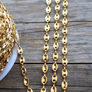 Op de afbeelding: Drie strengen van een gouden ovale ketting, plat liggend op een houten oppervlak.