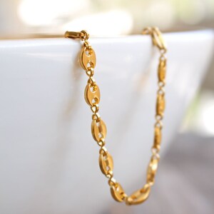 May include: A gold chain bracelet with a mariner link design. The bracelet is on a white surface.