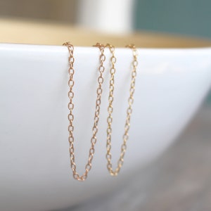 May include: Three gold chains hanging from the edge of a white bowl. The chains are made of small, oval-shaped links.