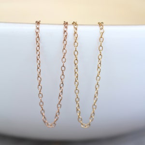 May include: Two delicate gold chains, one in rose gold and one in yellow gold, are displayed against a white background. The chains are both simple and elegant, making them perfect for layering or wearing alone.