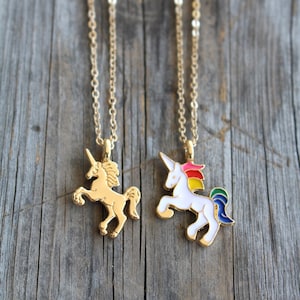 May include: Two gold necklaces with unicorn pendants. One pendant is gold and the other is white with a rainbow mane and tail.
