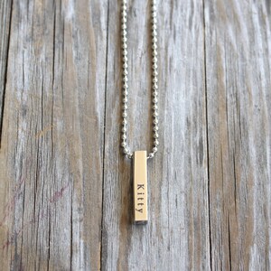 May include: A silver chain necklace with a silver bar pendant engraved with the name "Kitty".