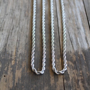 May include: Two silver rope chains on a wooden surface.
