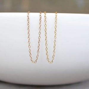 May include: Two gold chains, one slightly thicker than the other, are hanging from the edge of a white bowl.