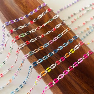 May include: A collection of colorful enamel chain links in various colors, including purple, red, green, blue, orange, yellow, and pink. The chains are laid out on a wooden surface.