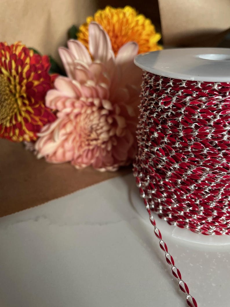 May include: A spool of red and silver chain with a white plastic spool. The chain is a flat, oval shape.
