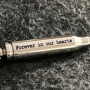Puede incluir: Un llavero de plata con forma de bala con un anillo y la inscripci&oacute;n "Forever in our hearts".