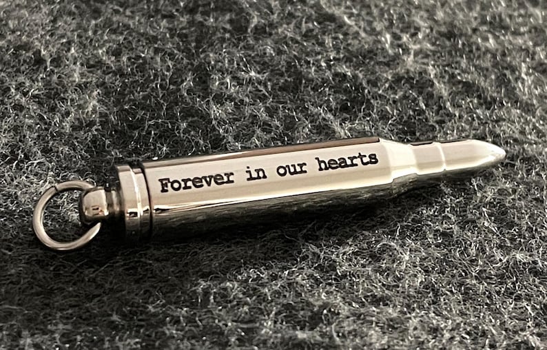 Puede incluir: Un llavero de plata con forma de bala con un anillo y la inscripci&oacute;n "Forever in our hearts".