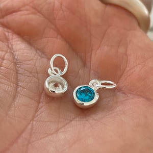 May include: Two silver charms, one with a clear crystal and one with a blue crystal.