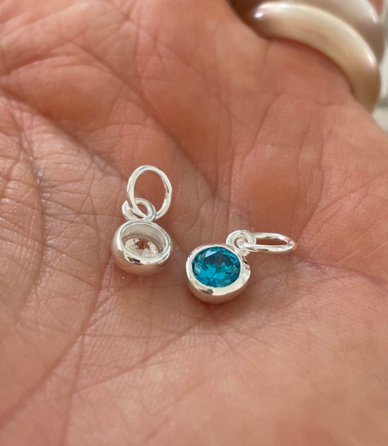 May include: Two silver charms, one with a clear crystal and one with a blue crystal.