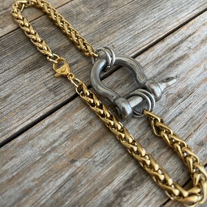Pu&ograve; includere: Una collana a catena dorata con una chiusura in metallo argentato e un grande anello in metallo argentato. L'anello ha un design decorativo ed &egrave; attaccato alla catena con un anello argentato pi&ugrave; piccolo.