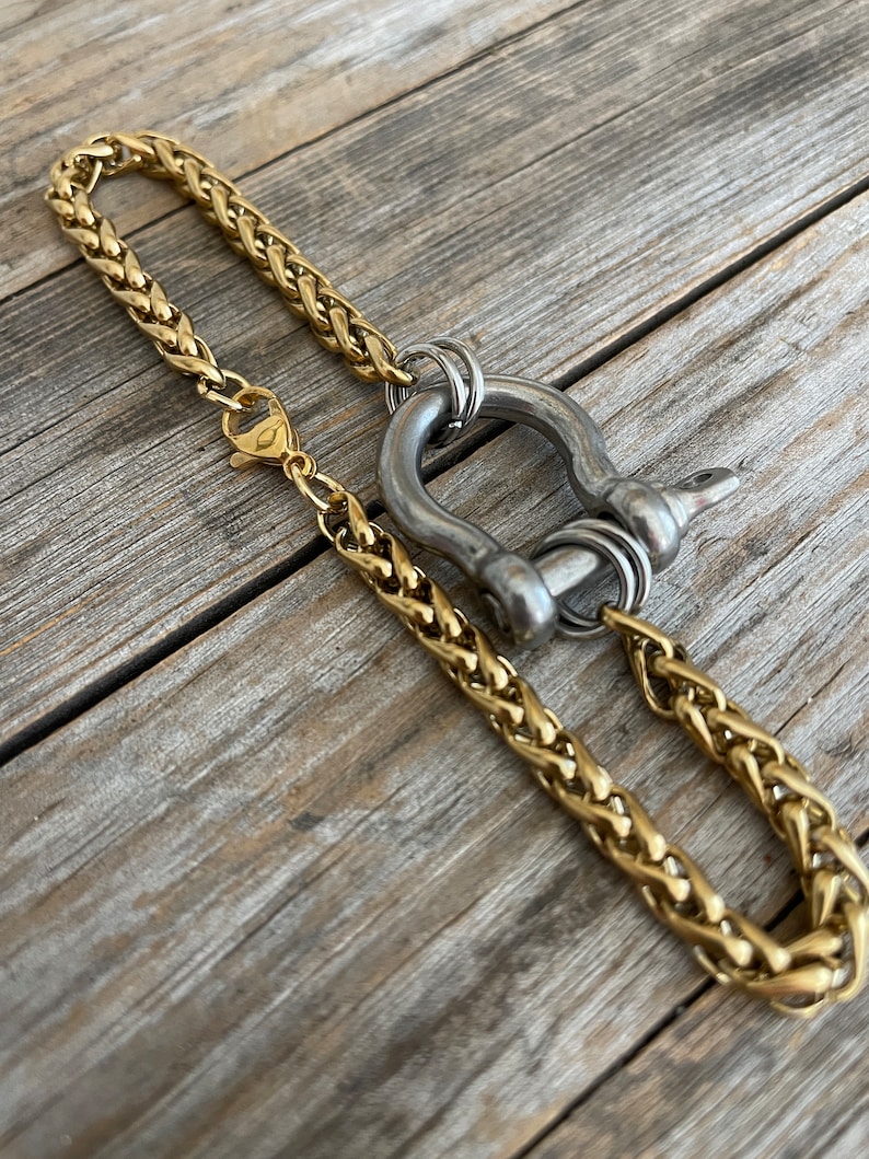 Pu&ograve; includere: Una collana a catena dorata con una chiusura in metallo argentato e un grande anello in metallo argentato. L'anello ha un design decorativo ed &egrave; attaccato alla catena con un anello argentato pi&ugrave; piccolo.