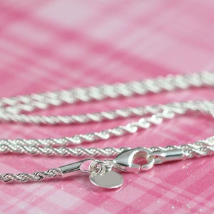 May include: A silver rope chain necklace with a small, round pendant. The chain is on a pink background.
