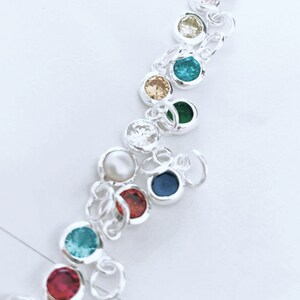 May include: A silver charm bracelet with colorful round gemstones. The bracelet features a variety of colors, including red, blue, green, yellow, and pink.