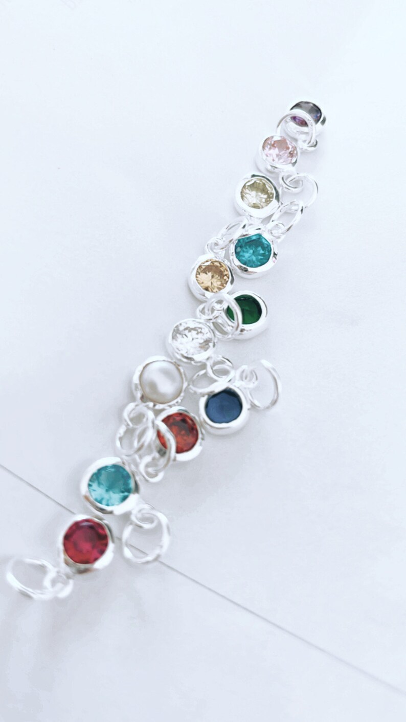 May include: A silver charm bracelet with colorful round gemstones. The bracelet features a variety of colors, including red, blue, green, yellow, and pink.