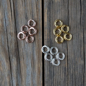 Pu&ograve; includere: Un set di sei anelli a salto in tre diverse finiture: oro rosa, oro e argento. Gli anelli sono disposti in tre gruppi di due su una superficie di legno.