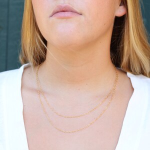 May include: A close-up of a person wearing a white shirt and a gold chain necklace. The necklace is layered with two chains.