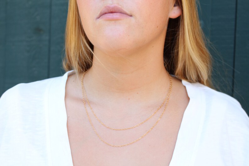 May include: A close-up of a person wearing a white shirt and a gold chain necklace. The necklace is layered with two chains.