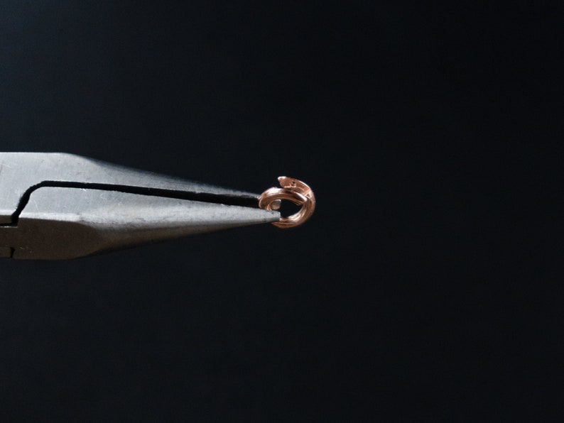 Pu&ograve; includere: Primo piano di un paio di pinze nere che tengono un piccolo anello di salto dorato.
