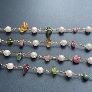 Puede incluir: Primer plano de varias hebras de joyer&iacute;a delicada. Cada hebra presenta una cadena dorada intercalada con perlas blancas y piedras preciosas de colores en tonos amarillos, verdes y rosas. El fondo es gris oscuro.