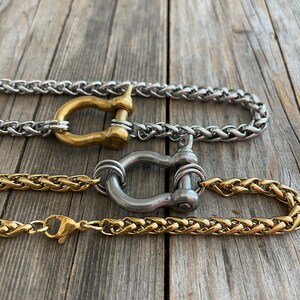 Pu&ograve; includere: Tre catene dorate e argentate con un designo di chiusura unico. Le catene sono intrecciate e hanno una finitura lucida. Le chiusure sono a forma di ferro di cavallo e hanno una finitura argentata.