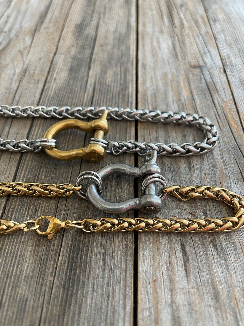Pu&ograve; includere: Tre catene dorate e argentate con un designo di chiusura unico. Le catene sono intrecciate e hanno una finitura lucida. Le chiusure sono a forma di ferro di cavallo e hanno una finitura argentata.