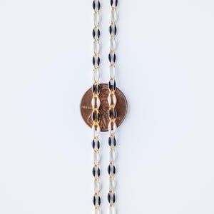 May include: A black and white chain necklace with gold accents. The chain is made of oval-shaped links. A penny is placed next to the chain to show the size.