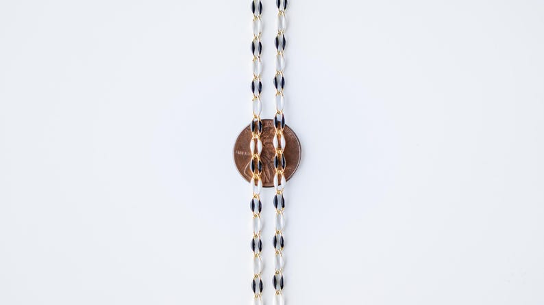 May include: A black and white chain necklace with gold accents. The chain is made of oval-shaped links. A penny is placed next to the chain to show the size.