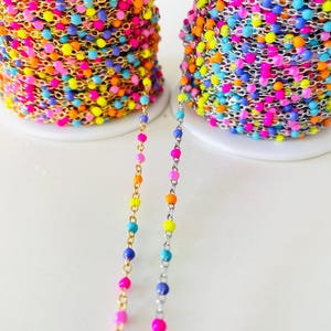 May include: Two spools of colorful beaded chain. One spool has gold-colored chain with multi-colored beads, and the other has silver-colored chain with multi-colored beads. The beads are in shades of pink, yellow, blue, and orange.