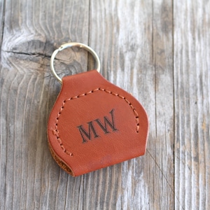 May include: A brown leather keychain with a stitched edge and a silver key ring. The keychain has the initials "MW" engraved on the front.