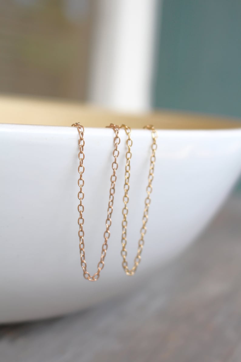 May include: Three gold chains hanging from the edge of a white bowl. The chains are made of small, oval-shaped links.