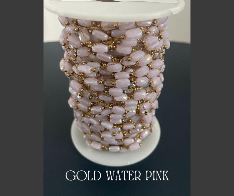 May include: A spool of gold-toned wire wrapped with light pink, faceted beads. The beads are strung together with gold wire. The text "GOLD WATER PINK" is at the bottom of the image.