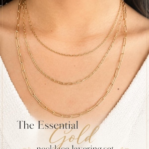 May include: A gold necklace layering set consisting of three chains of varying lengths, specifically 16, 17, and 20 inches, each featuring a 2-inch extender. The text reads: SHINY LITTLE BLESSINGS PRESENTS, The Essential Gold necklace layering set.